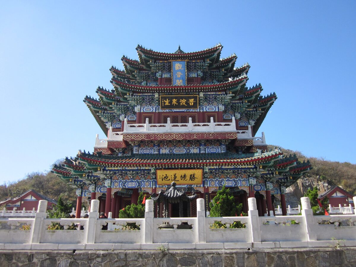 A tall hall with many stacked, green-tiled roofs and colorful painted eaves behind a white stone balustrade at Tianmenshan Temple