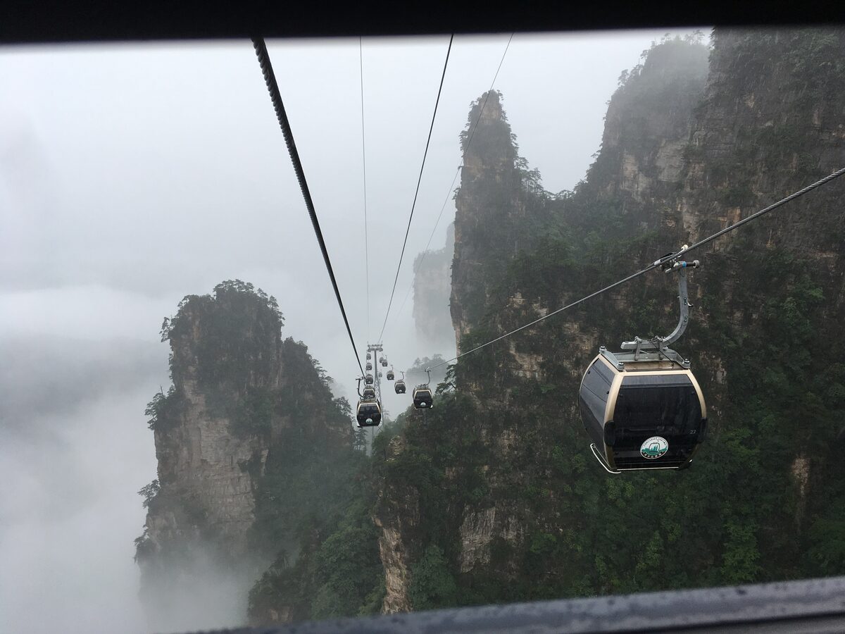 A cable car gondola on its cable between misty sandstone pillars on Tianzi Mountain