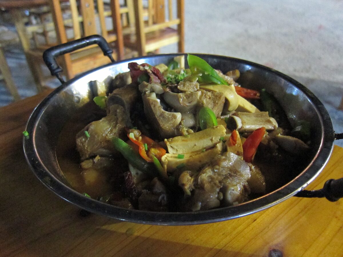 A steel pot of sanxiaguo stew, meat on the bone with tofu and green and red peppers, on a restaurant table in Wulingyuan