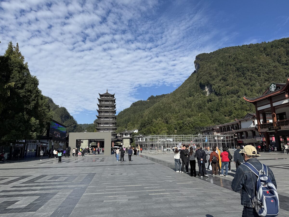 The paved square at the Wulingyuan entrance with visitors walking toward a pagoda tower and forested hills behind