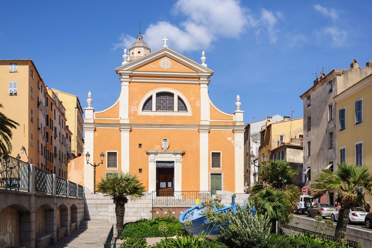 The orange baroque facade of the cathedral at the top of a steep street, with palm trees in front