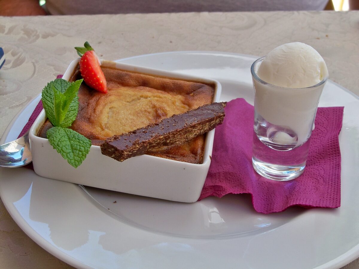 A baked chestnut flan in a white dish with a chocolate bar, a strawberry and mint, and a scoop of ice cream in a small glass