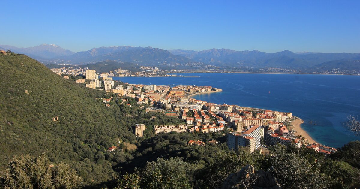 Ajaccio and its gulf from the hills to the west on a clear day: the old town on its point, a sandy beach, deep blue water and the mountains of the interior behind