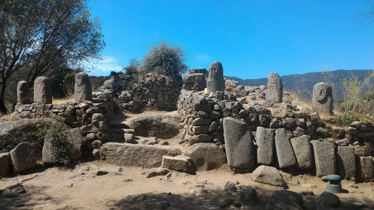 Standing menhirs and stone walls at the Filitosa site, with a grassy field and trees around