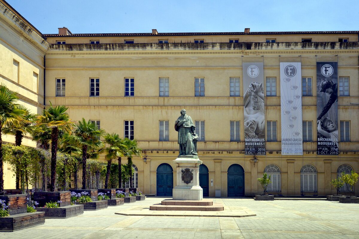 The yellow facade of the Palais Fesch, with the statue of Cardinal Fesch in the square and banners on the wall