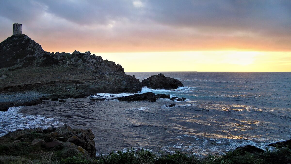 Sunset over dark rocks at the Parata, with the Genoese tower on the headland at left