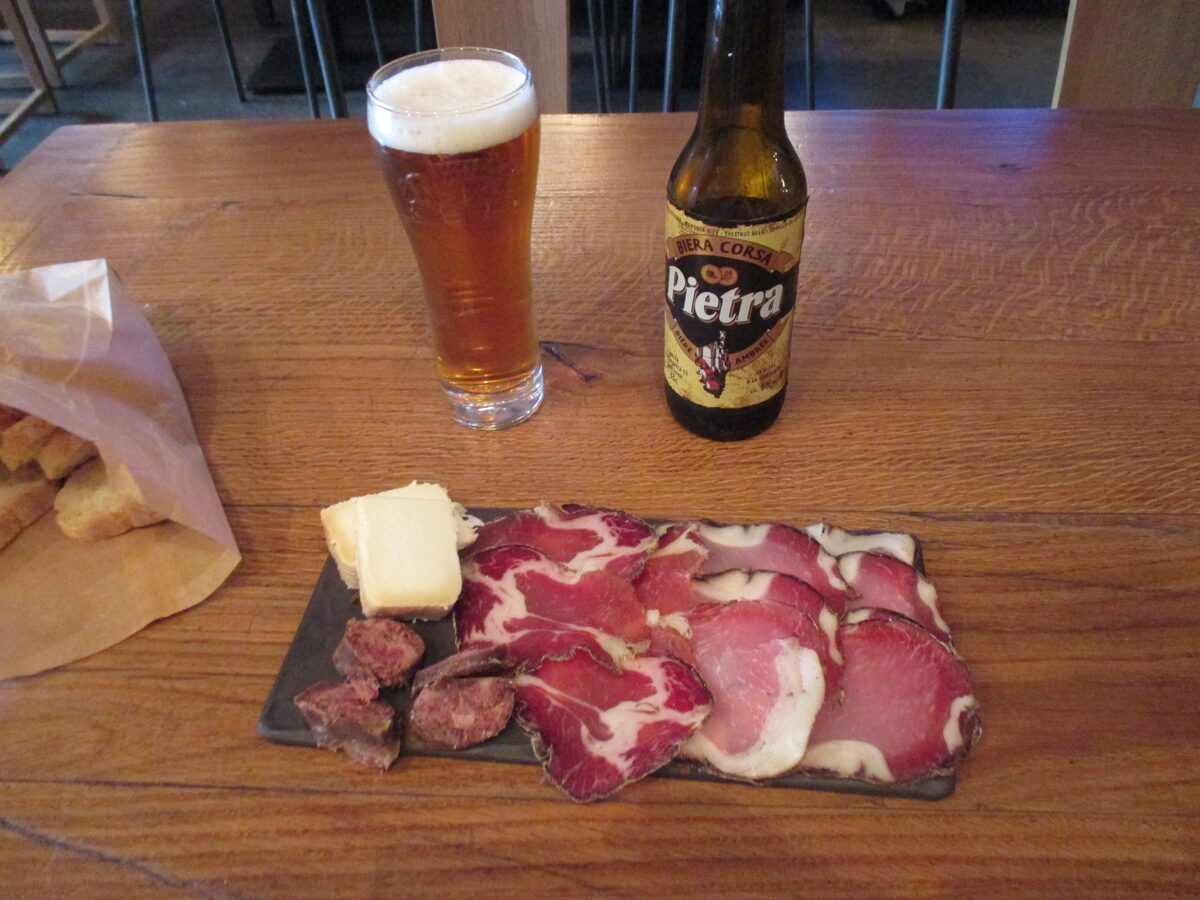 A glass of Pietra beer beside a board of cured meat and cheese