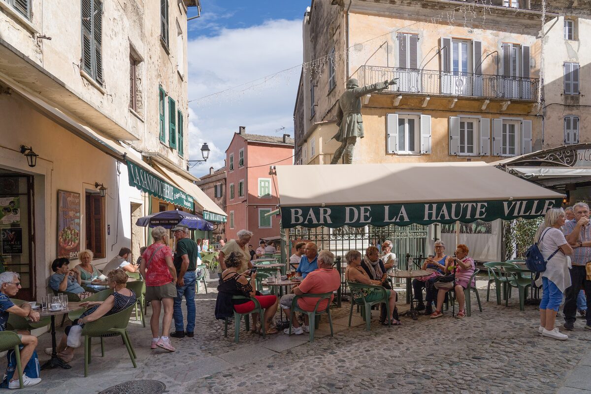 The café terrace of the Bar de la Haute Ville on the Place Gaffory in Corte's old town, with a bronze statue on the wall above