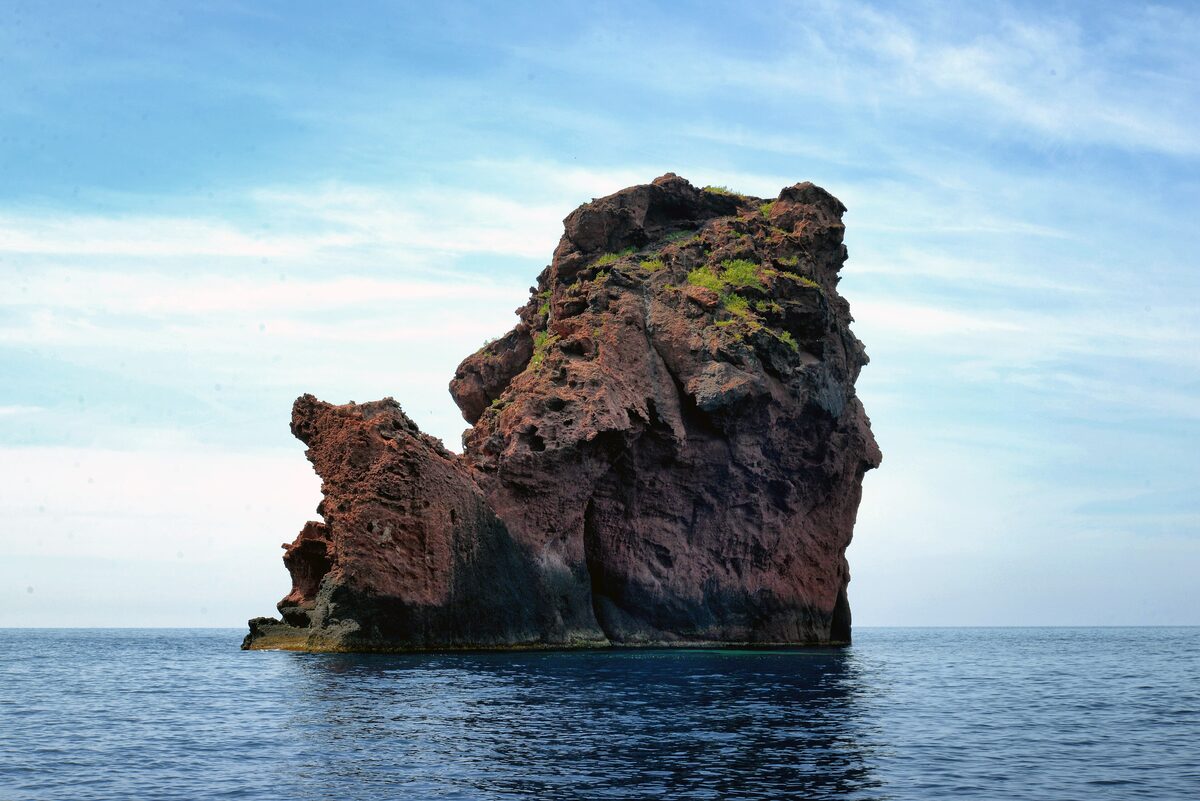 The red volcanic rock of the Îlot Palazzu rising from the open sea off Punta Palazzu inside the Scandola reserve, seen from a boat