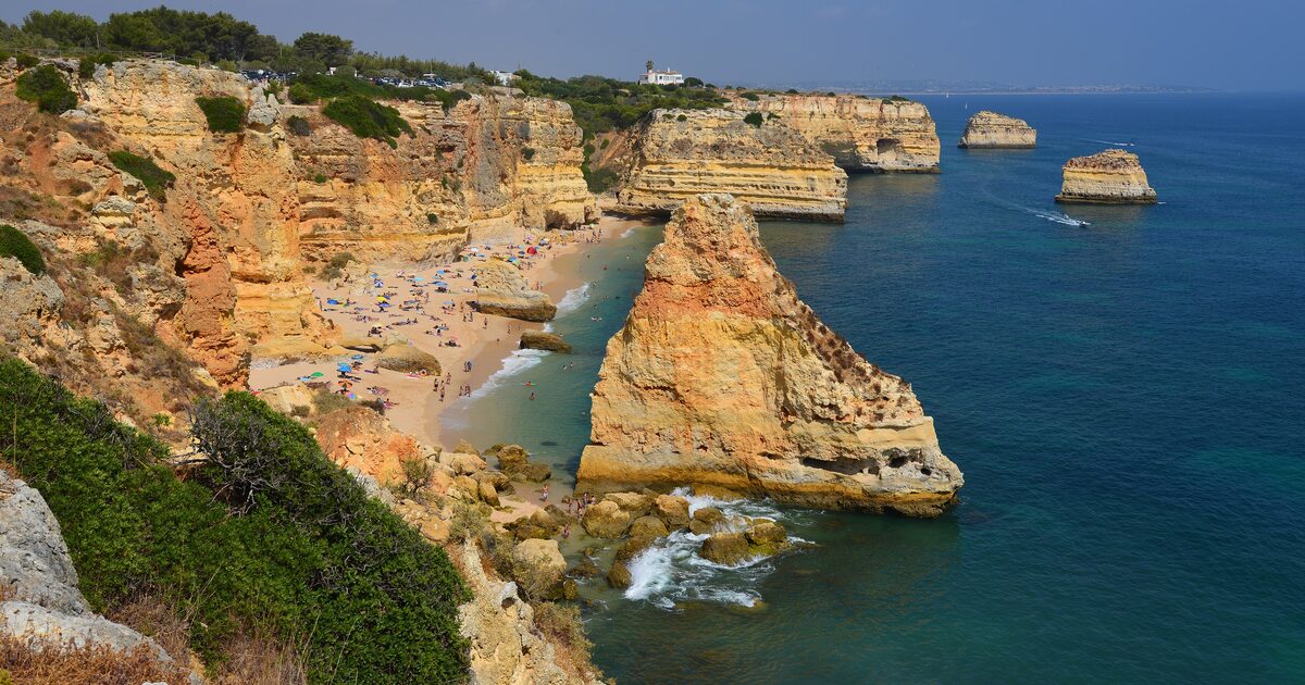 Golden cliffs, sea stacks and a sandy cove full of sunbathers at Praia da Marinha on the Algarve