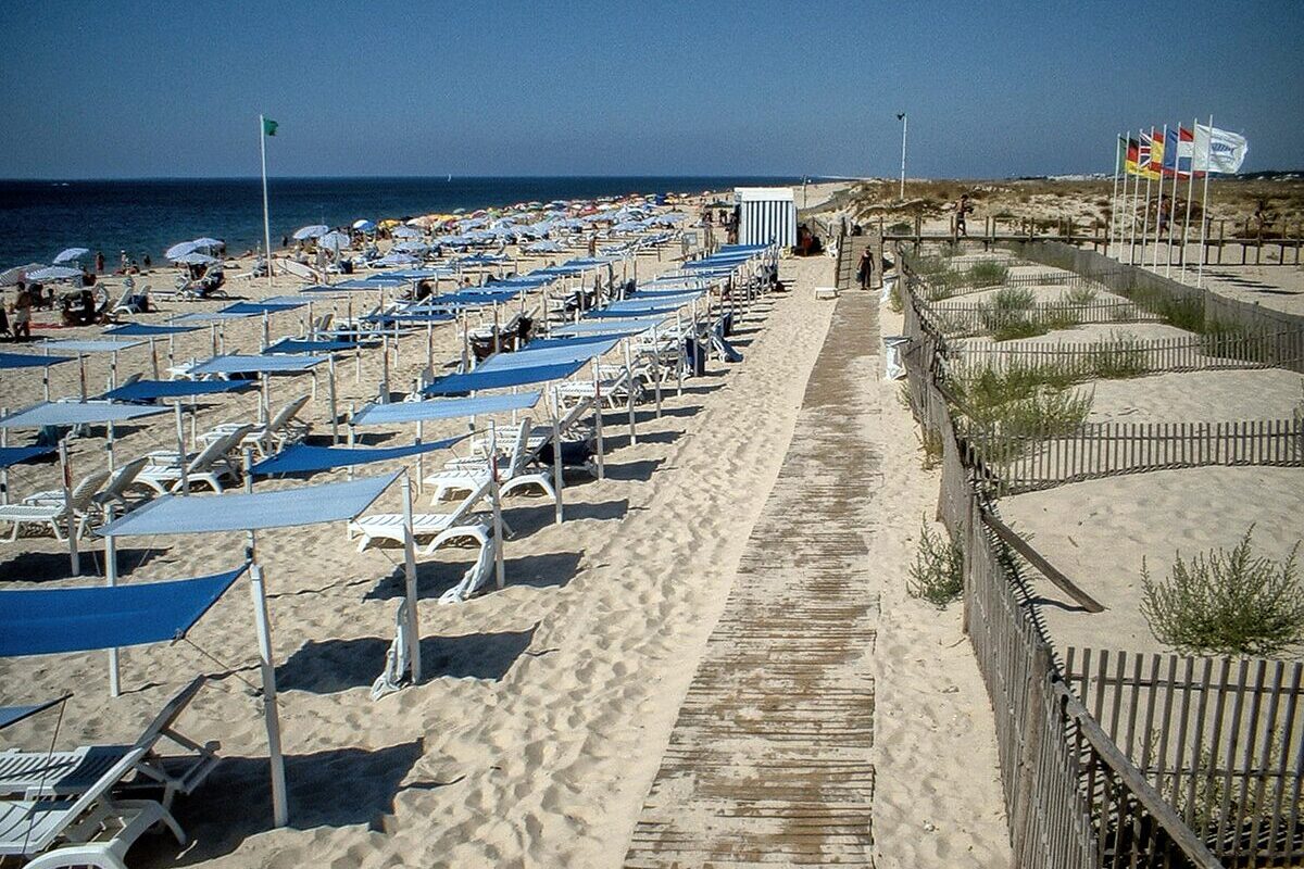 Sunbeds and blue awnings along a boardwalk at Praia do Barril on the Ilha de Tavira, under a clear sky