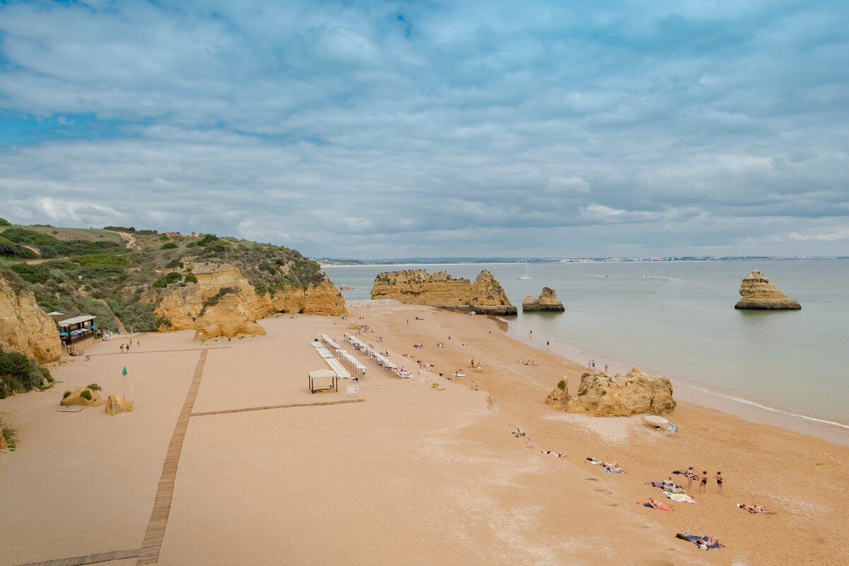 Sandy beach with golden cliffs and rock stacks on a sunny day in the Lagos area