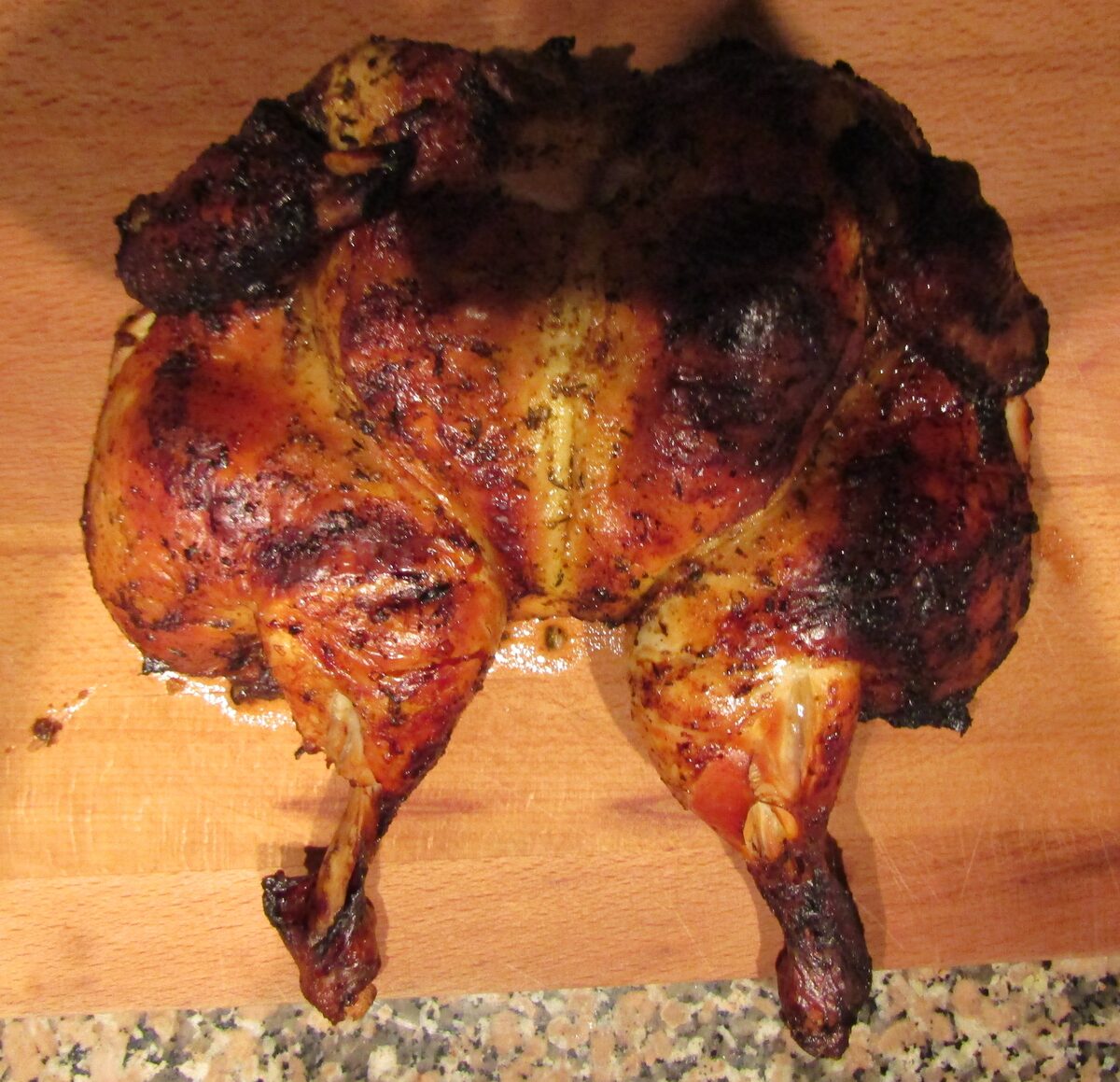 Butterflied piri-piri chicken, browned and charred on a wooden board