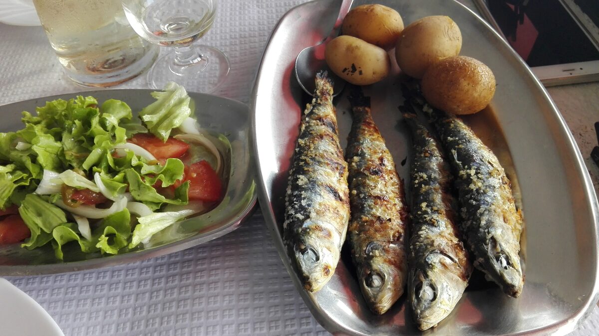 A tray of four grilled sardines with boiled potatoes and a green salad