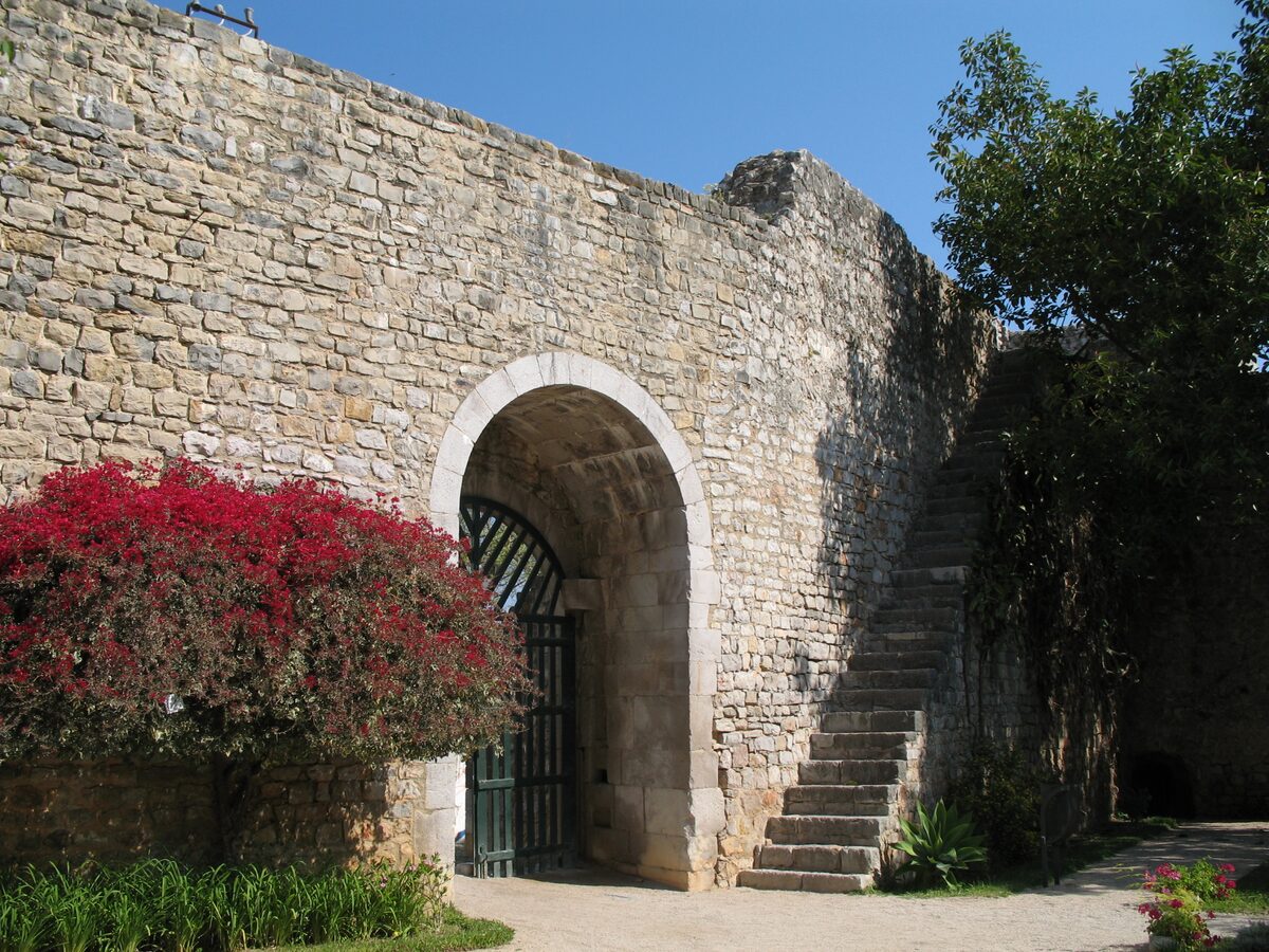 The stone walls of Tavira castle with an arched gateway, stairs and red bougainvillea
