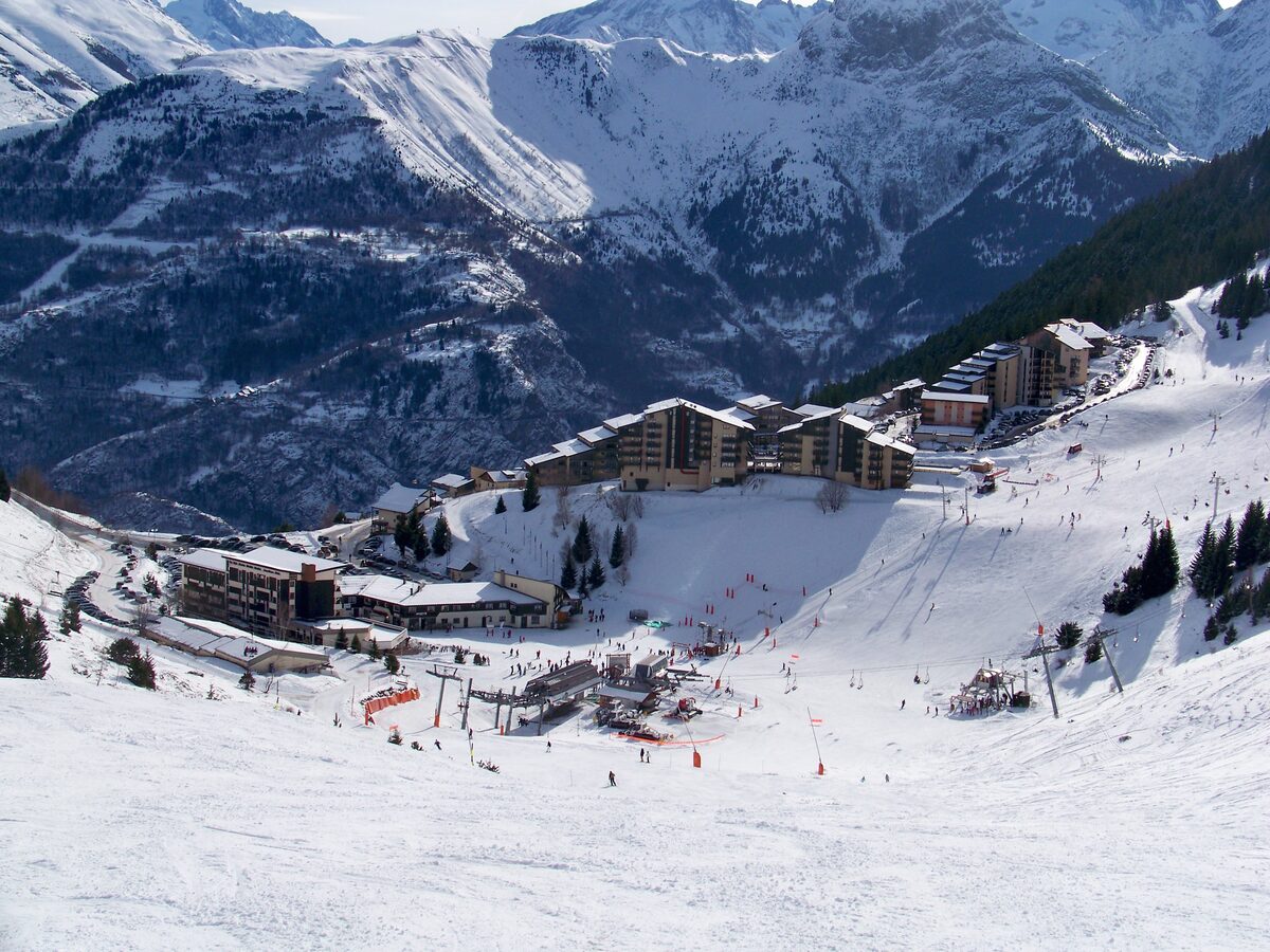 The Auris village and its beginner pistes in snow, with skiers and the lift poles on the lower slope