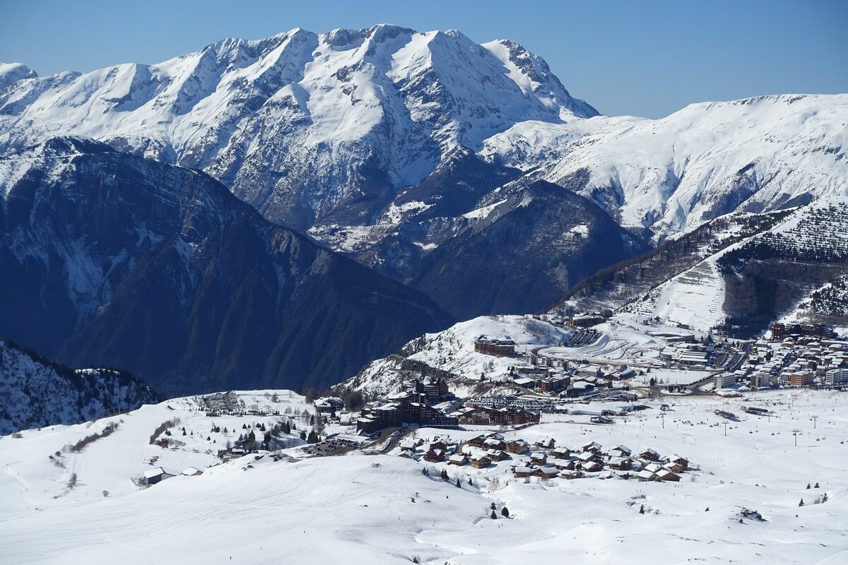 The village of Alpe d'Huez in snow seen from above, with a high snowy massif rising behind it