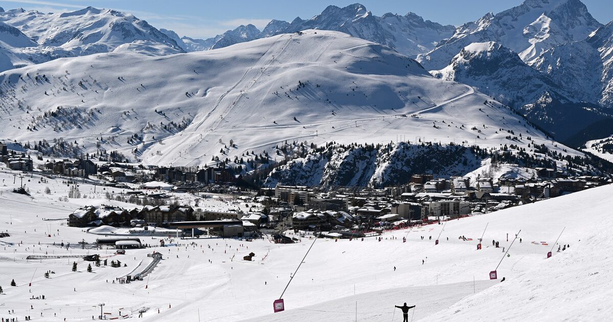 The village of Alpe d'Huez under snow, with its pistes and a lift station in front and the mountains behind