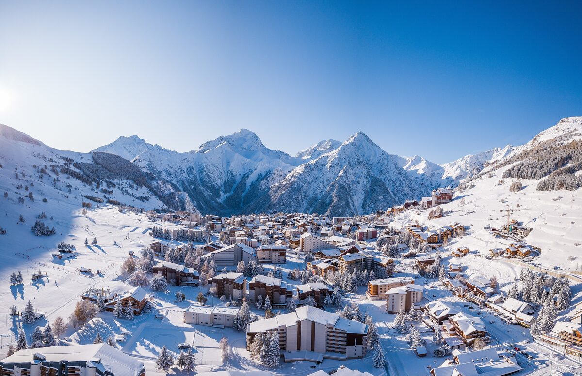 The Les Deux Alpes village in snow, with its rooftops and the high mountains behind
