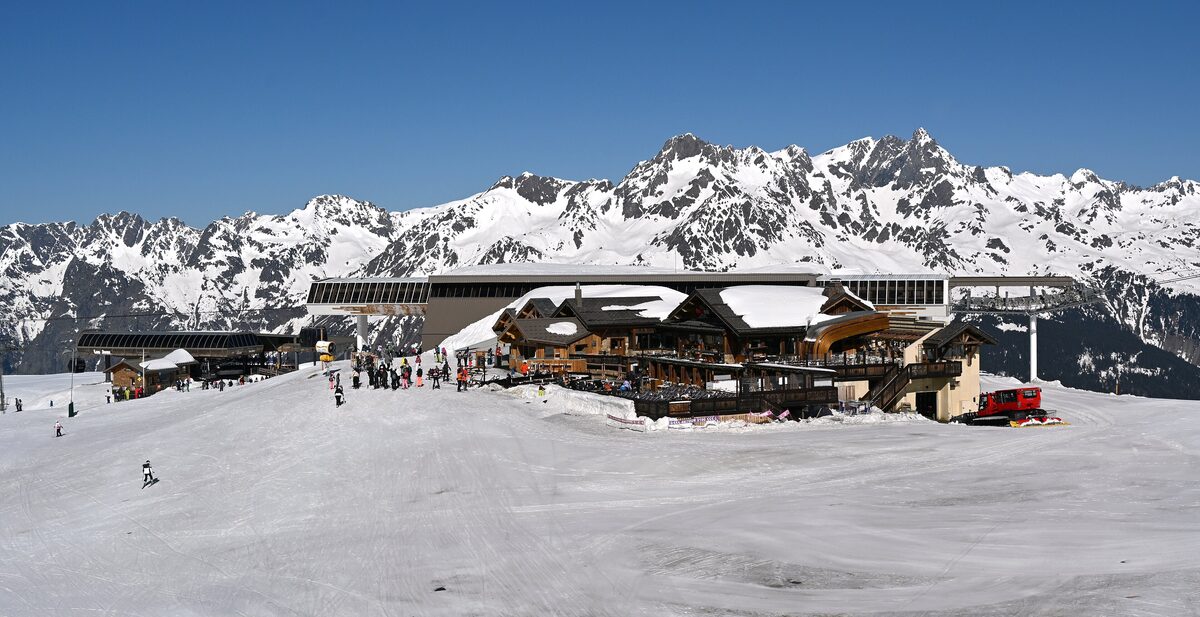 The Les Jeux 2100 lift station in snow above Alpe d'Huez, with skiers and a restaurant terrace at the top of the slopes