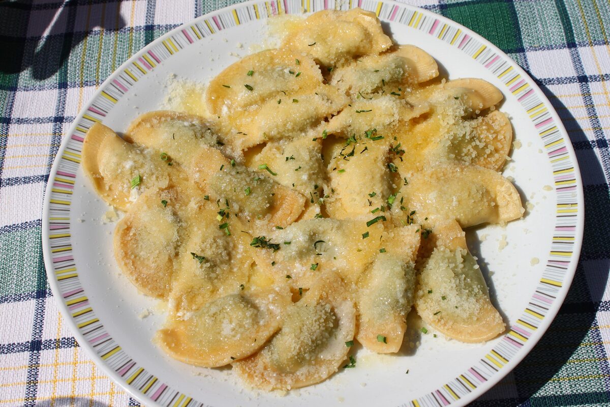 Half-moon pasta with a green spinach filling, topped with melted butter, herbs and grated cheese