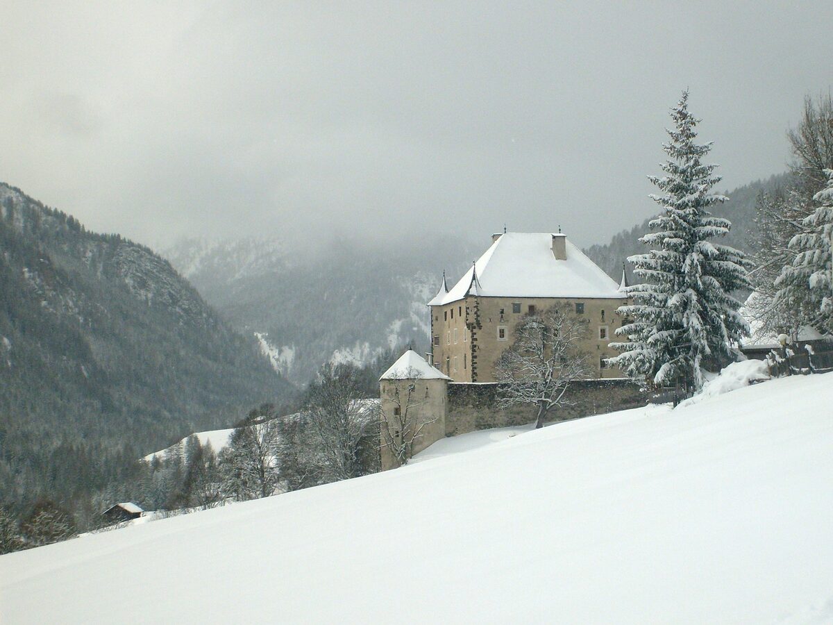 Ciastel Colz, a stone castle with snow on its steep roof and on the slope below, among winter pines