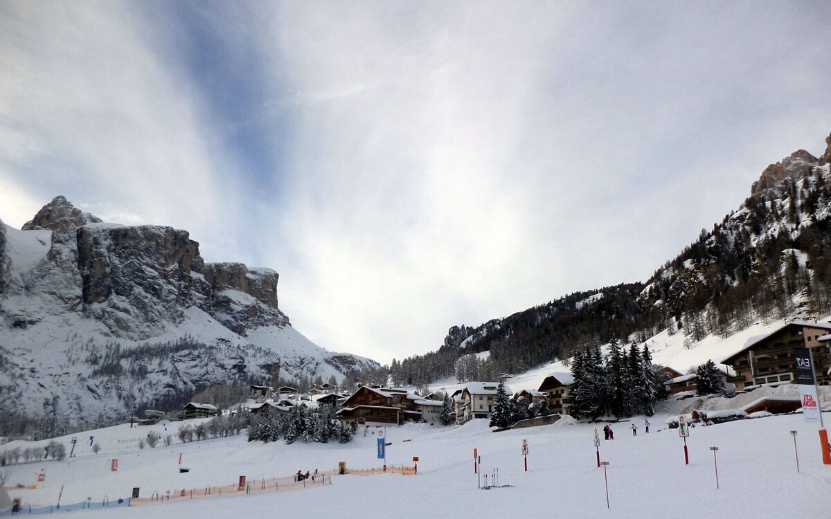 Chalets and ski runs in the snow at Colfosco, with a rocky massif rising behind the village