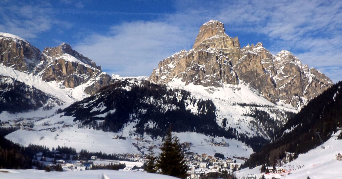 Snow-covered Corvara village at the foot of a rocky Dolomite peak, under a blue winter sky in Alta Badia