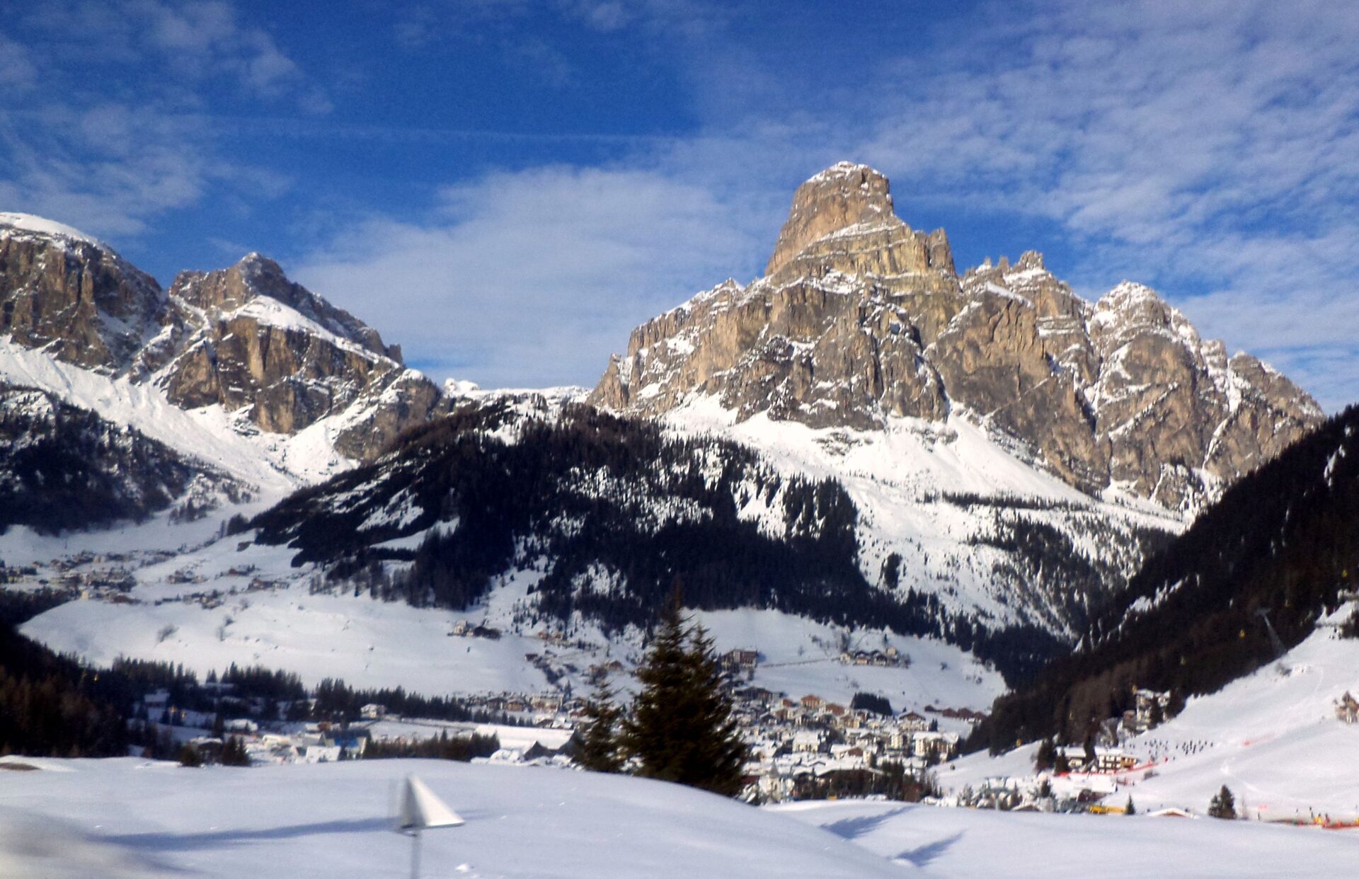 Snow-covered Corvara village at the foot of a rocky Dolomite peak, under a blue winter sky in Alta Badia