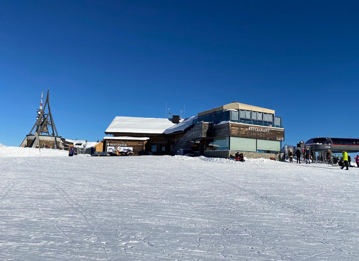 The Kronplatz summit with a restaurant, a lift station and groomed snow under a clear blue winter sky