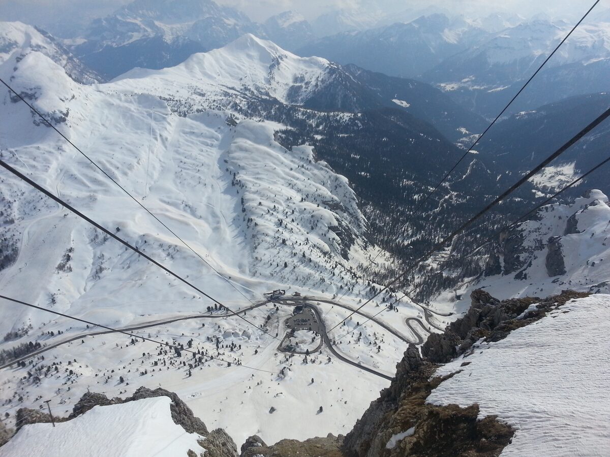 Looking down from the Lagazuoi cable car cables over snowy slopes to the Falzarego Pass road and its hairpins