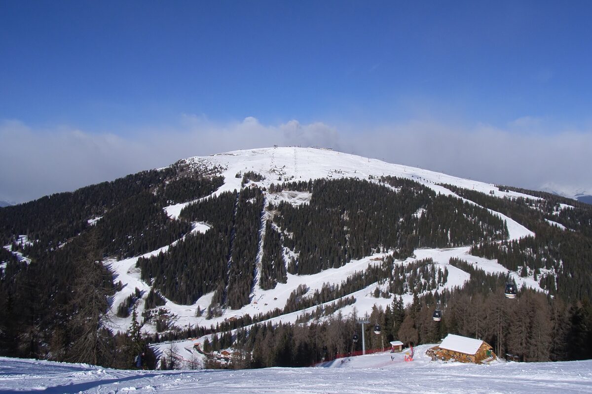 Groomed ski pistes on the south side of the Kronplatz, with a lift line running above the forest