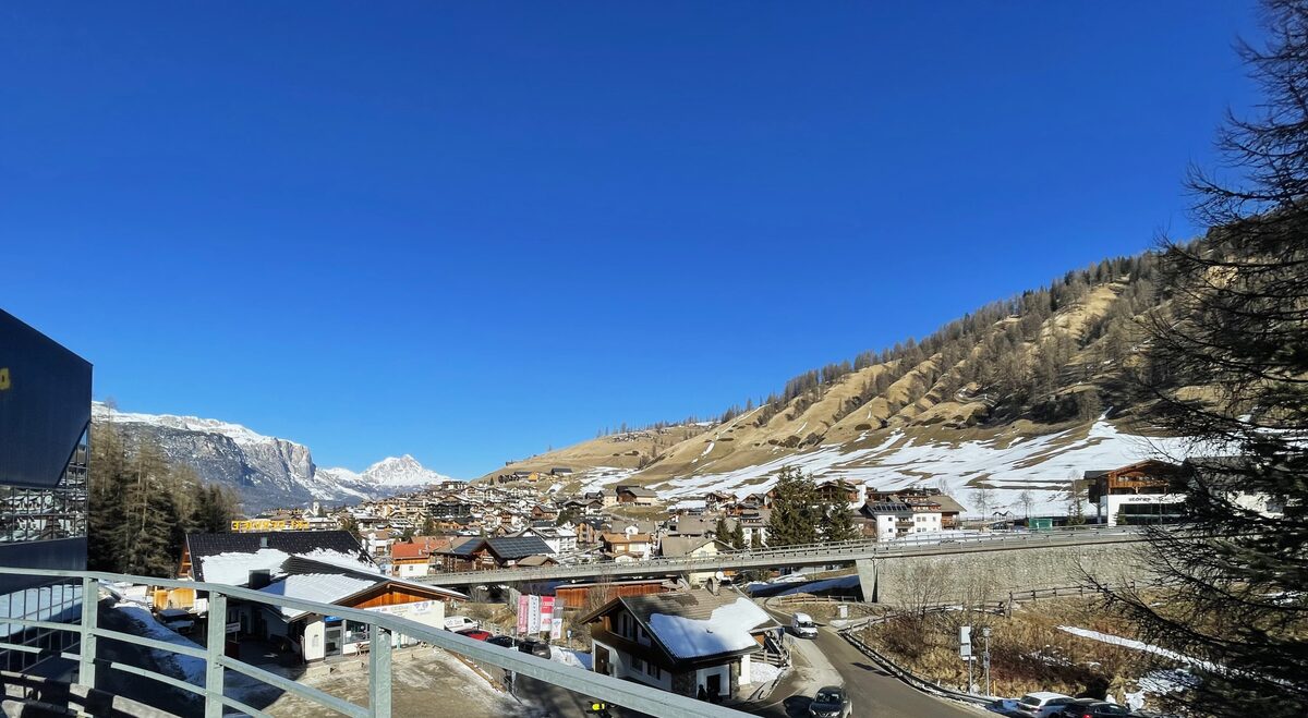 San Cassiano in late winter, with patches of snow on the brown hillsides above the village under a clear blue sky
