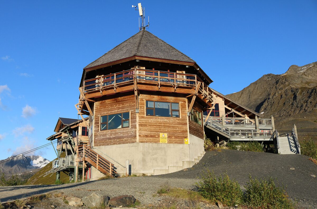 The timber Roundhouse building at the top of the Alyeska tram under a blue sky, with mountains behind
