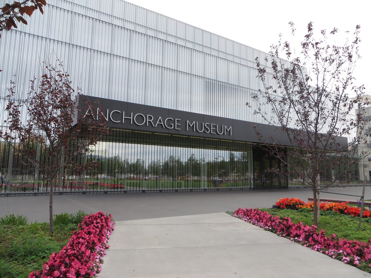 The glass-fronted Anchorage Museum at Rasmuson Center with flower beds in bloom in front of the entrance