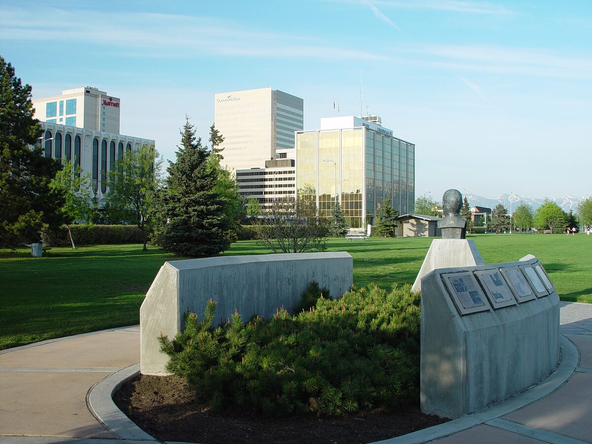 Downtown Anchorage office towers behind a green lawn in Delaney Park on a clear spring day