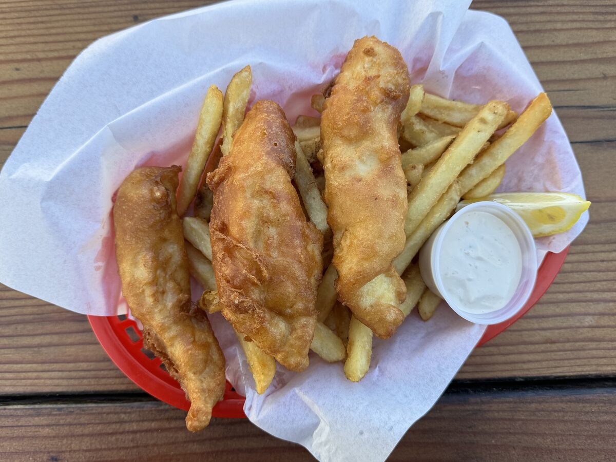 A basket of beer-battered halibut and chips with tartar sauce and a lemon wedge