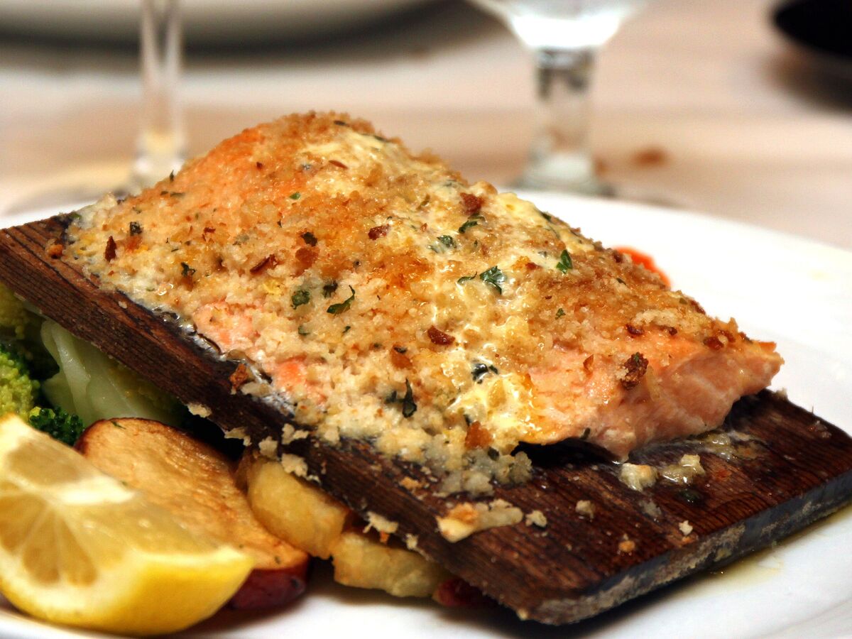 A salmon fillet baked with a herb crust on a cedar plank, served with broccoli and a lemon wedge