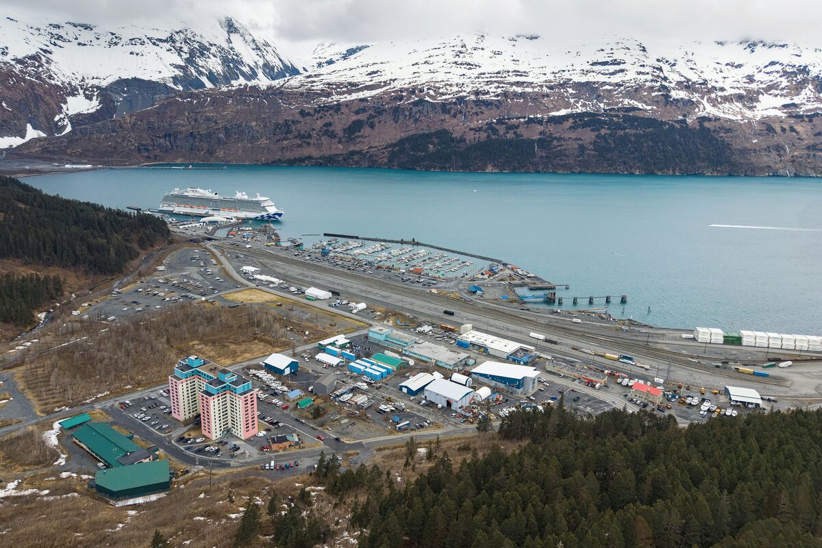Aerial view of Whittier with the Begich Towers, the small boat harbor, a cruise ship and snow-capped mountains over Prince William Sound