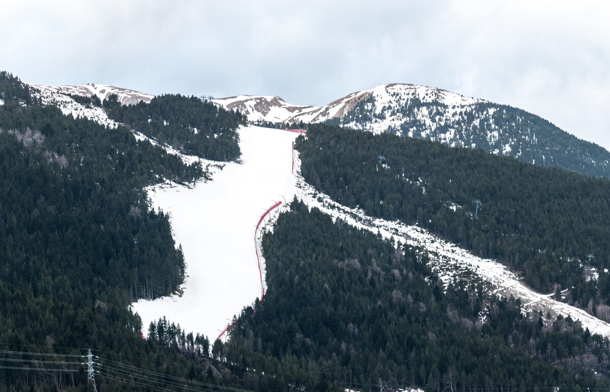 The snowy Àliga slope in El Tarter, a wide white run with red race netting cutting down through dark pine forest