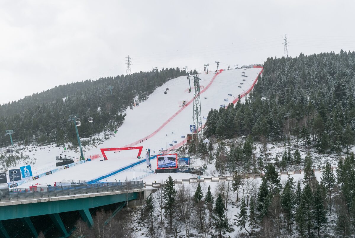 Red race gates and a blue finish area on the snowy Avet slope in Soldeu, with a gondola cabin passing above the piste