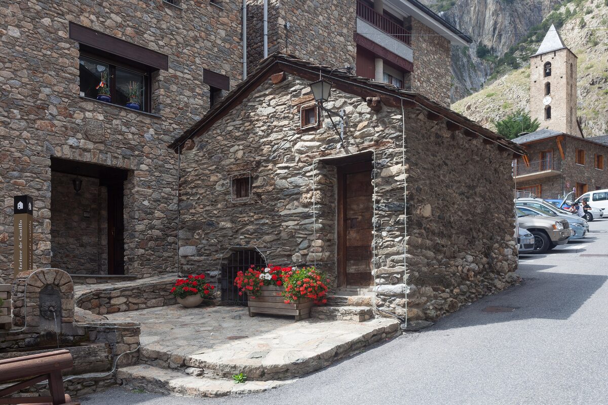Old stone houses on a small square in Canillo, with flower pots by the doorway and parked cars along the road