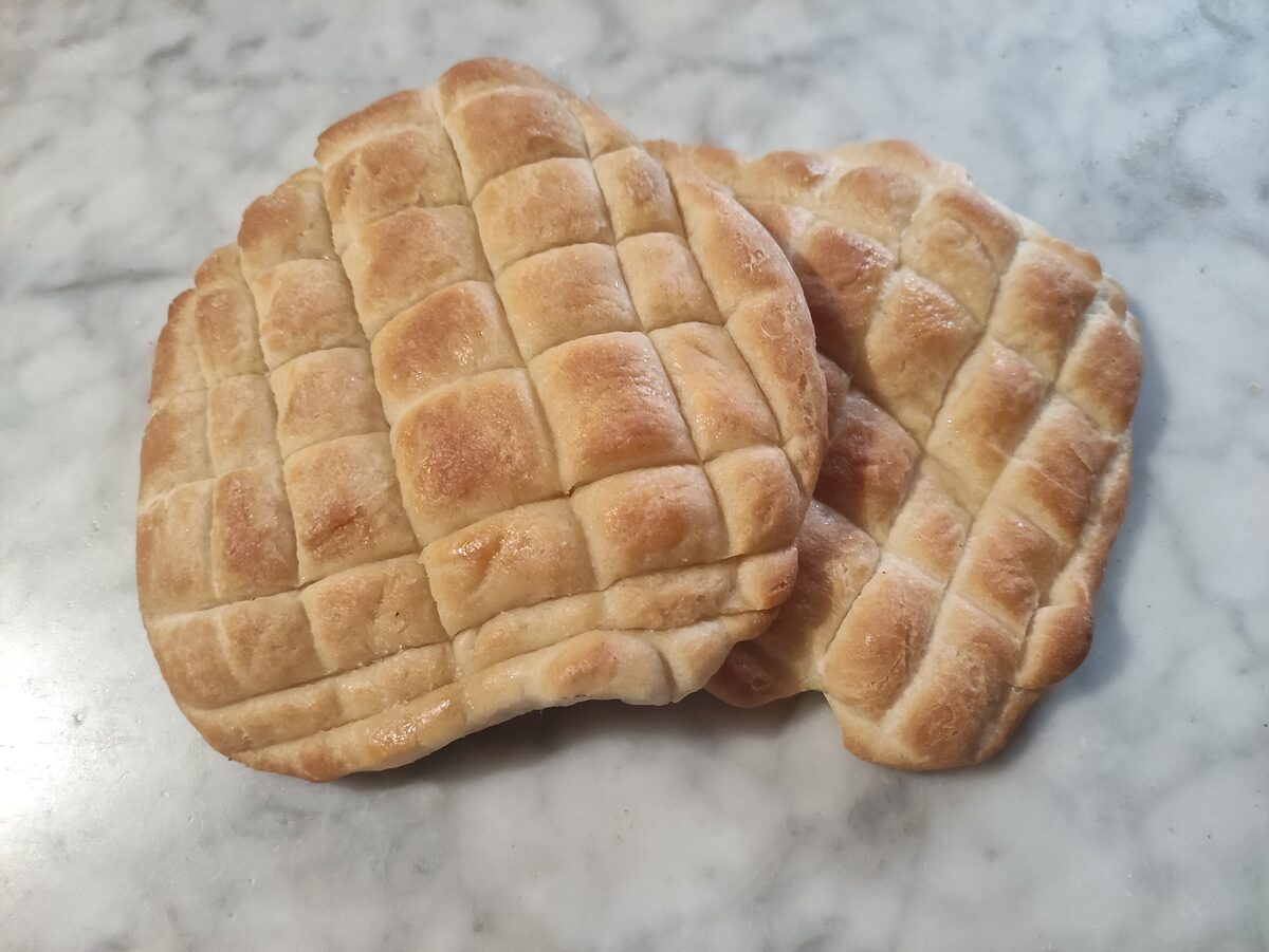 A flat coca bread with a crosshatch pattern, brushed with olive oil and sprinkled with salt