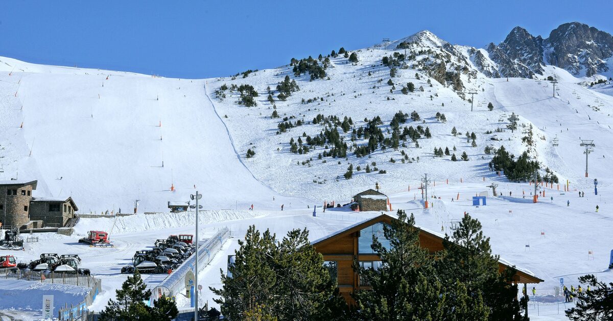 Groomed snowy pistes, lift towers and a wooden chalet at the foot of the slopes in Grandvalira under a clear blue sky