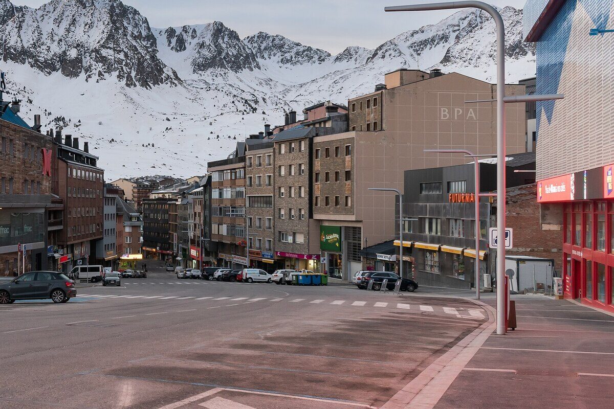 A street of shops and hotel blocks in Pas de la Casa with snowy peaks rising behind the roofs