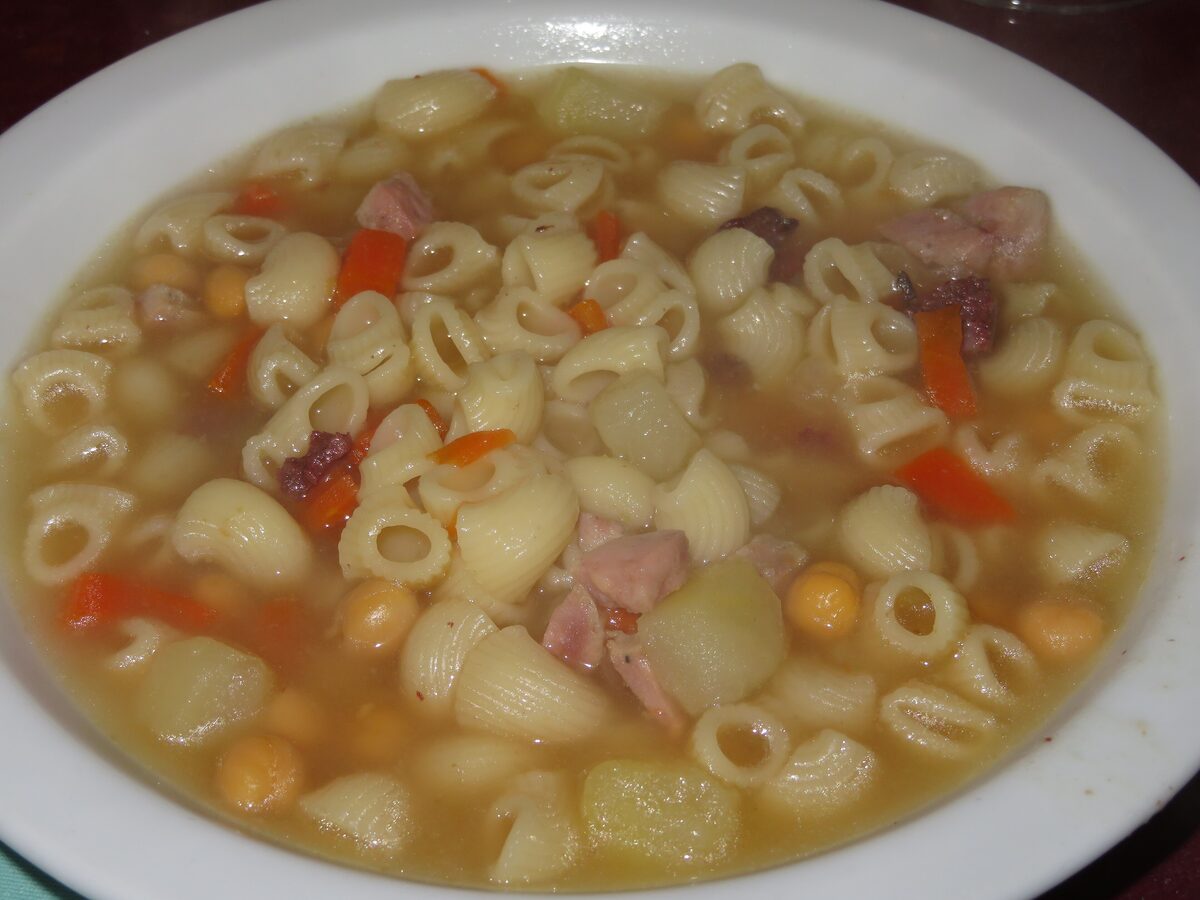 A bowl of escudella soup with small pasta, chickpeas, carrot and pieces of meat