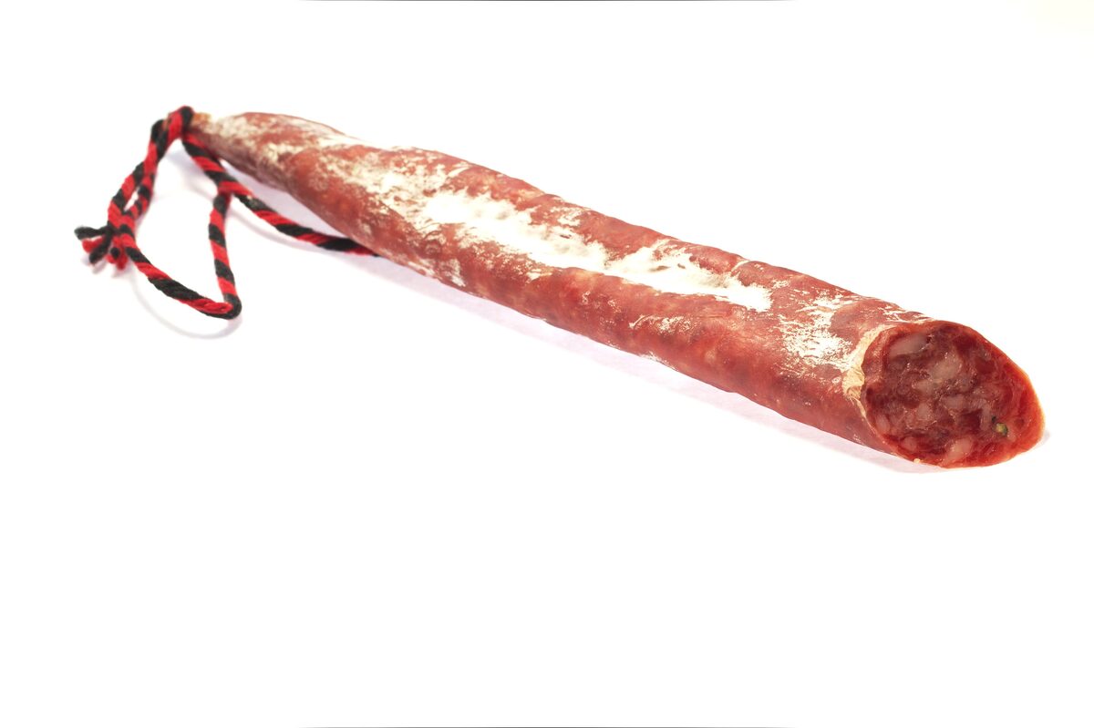 A thin cured fuet sausage with a red and black string tied at one end, on a white background