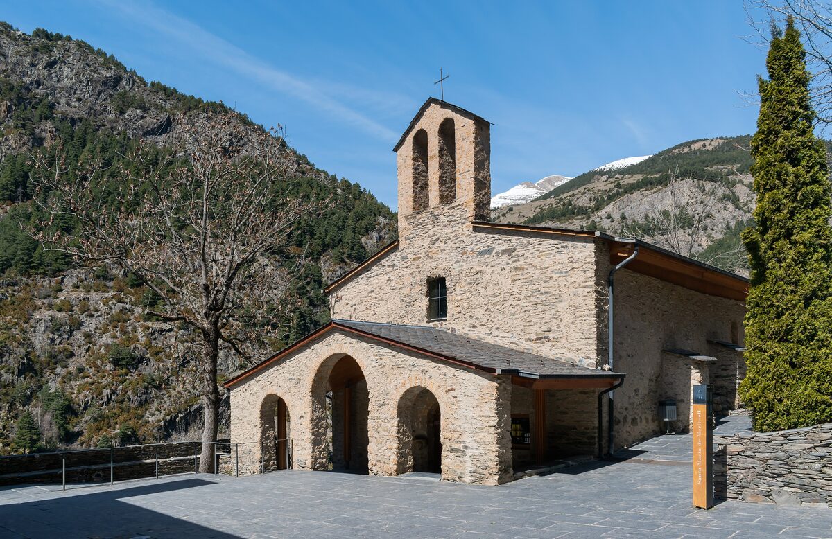 The stone Sanctuary of Meritxell with its bell tower and arcaded porch at the foot of a forested valley