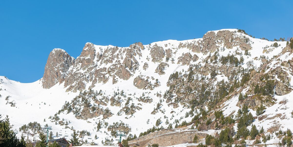 Snow-covered rocky peaks of the Arcalís mountains under a clear blue sky, with chairlift pylons at the foot of the slope