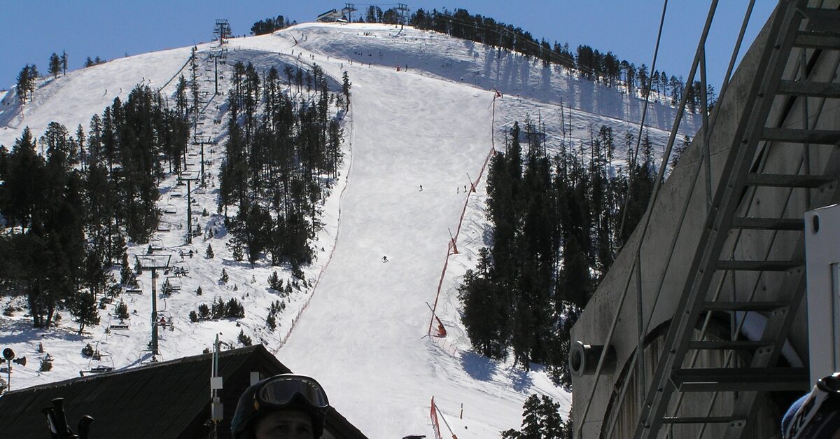 A groomed Pal Arinsal run between pines with a chairlift alongside, seen from beside a lift station at the bottom